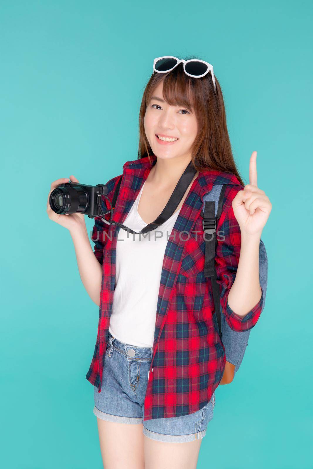 Beautiful young asian woman presenting travel trip summer with pointing something isolated on blue background, girl having activity hobby take a photo holding camera, journey in vacation and holiday. by nnudoo