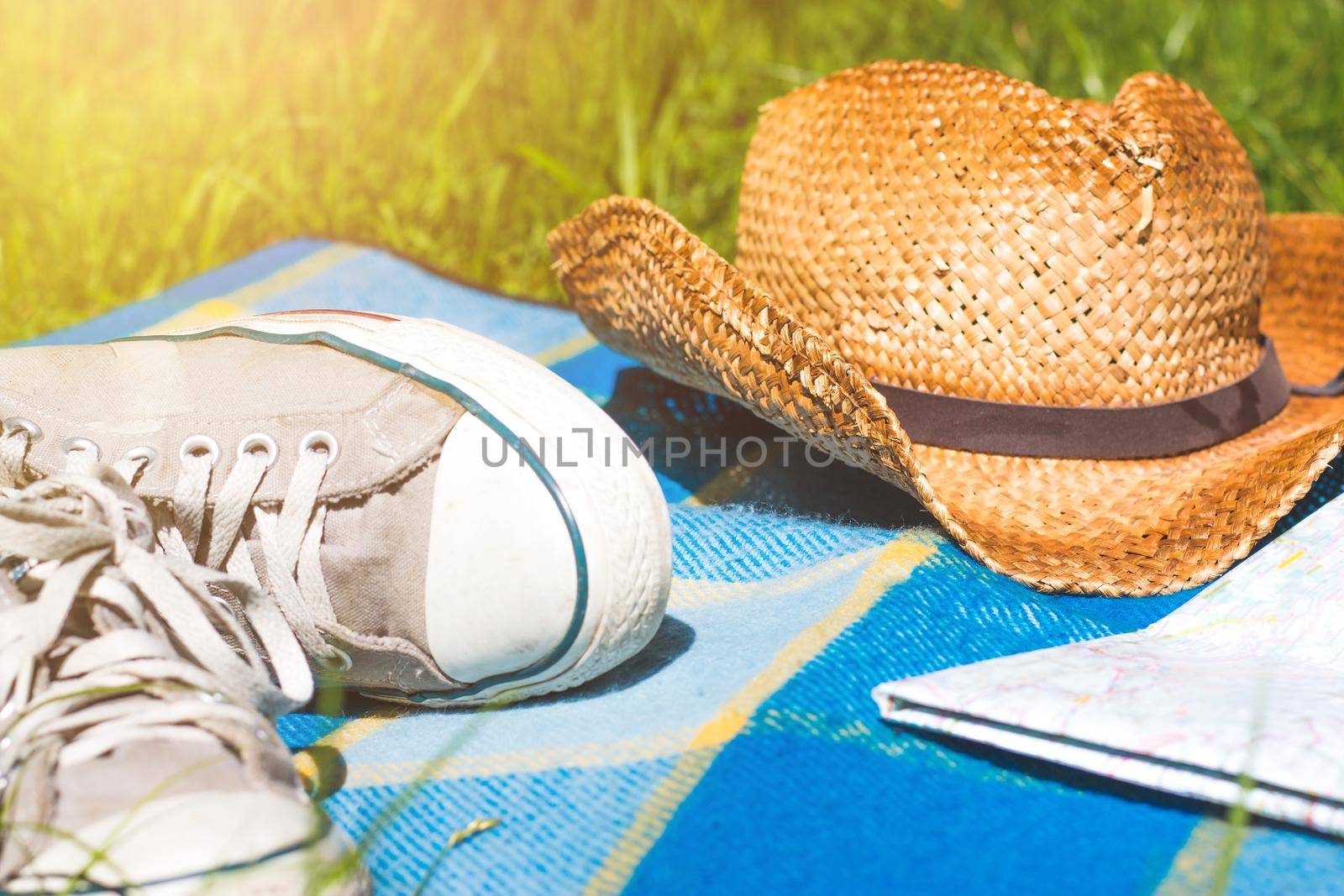 Picnic blanket with sneakers, map and straw hat