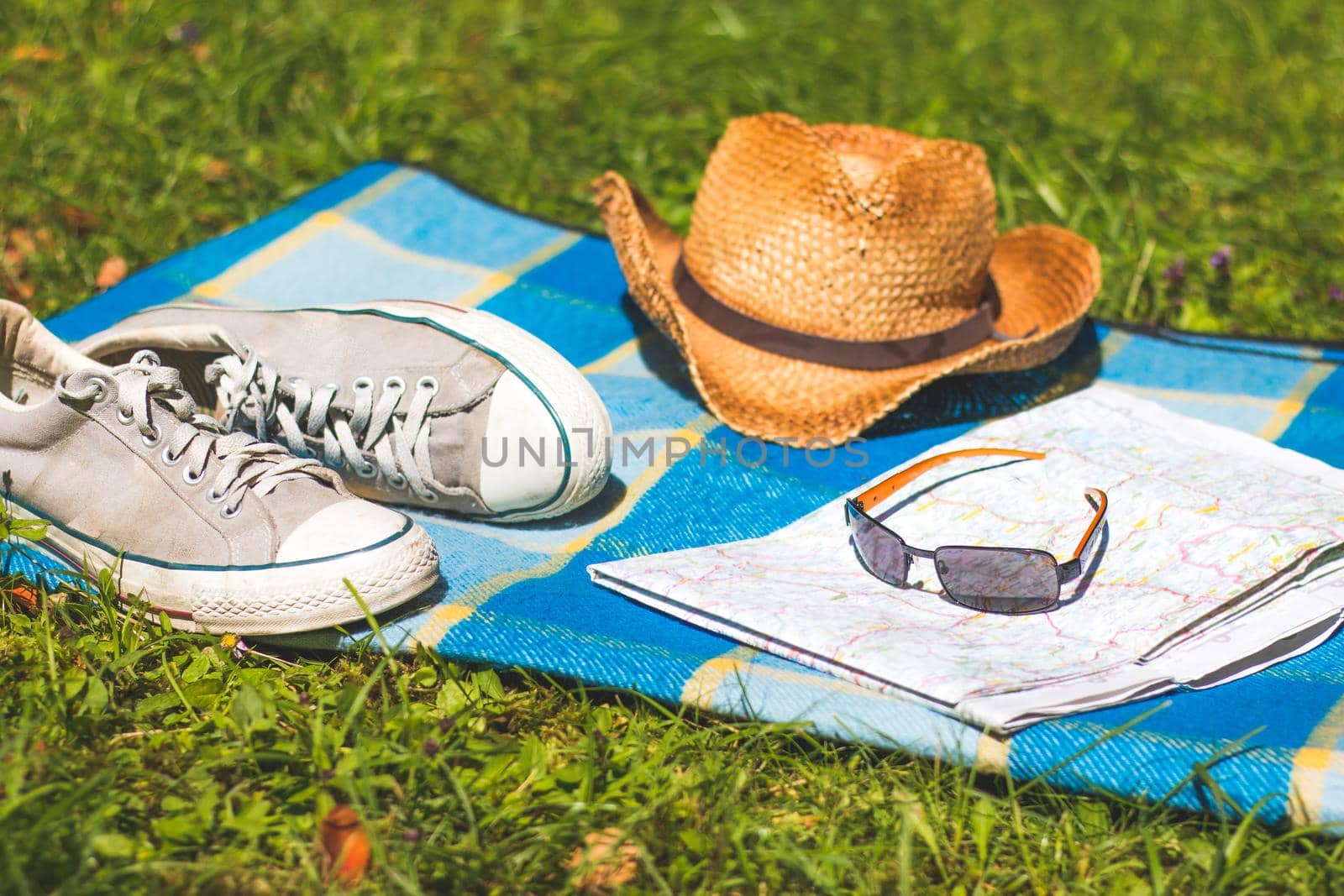 Picnic blanket with sneakers, straw hat, map and radio