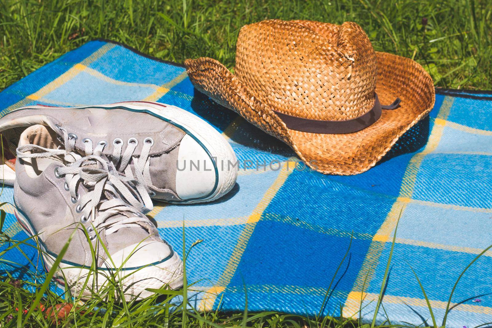 Chilling in the summer concept: picnic blanket with sneakers and straw hat by Daxenbichler