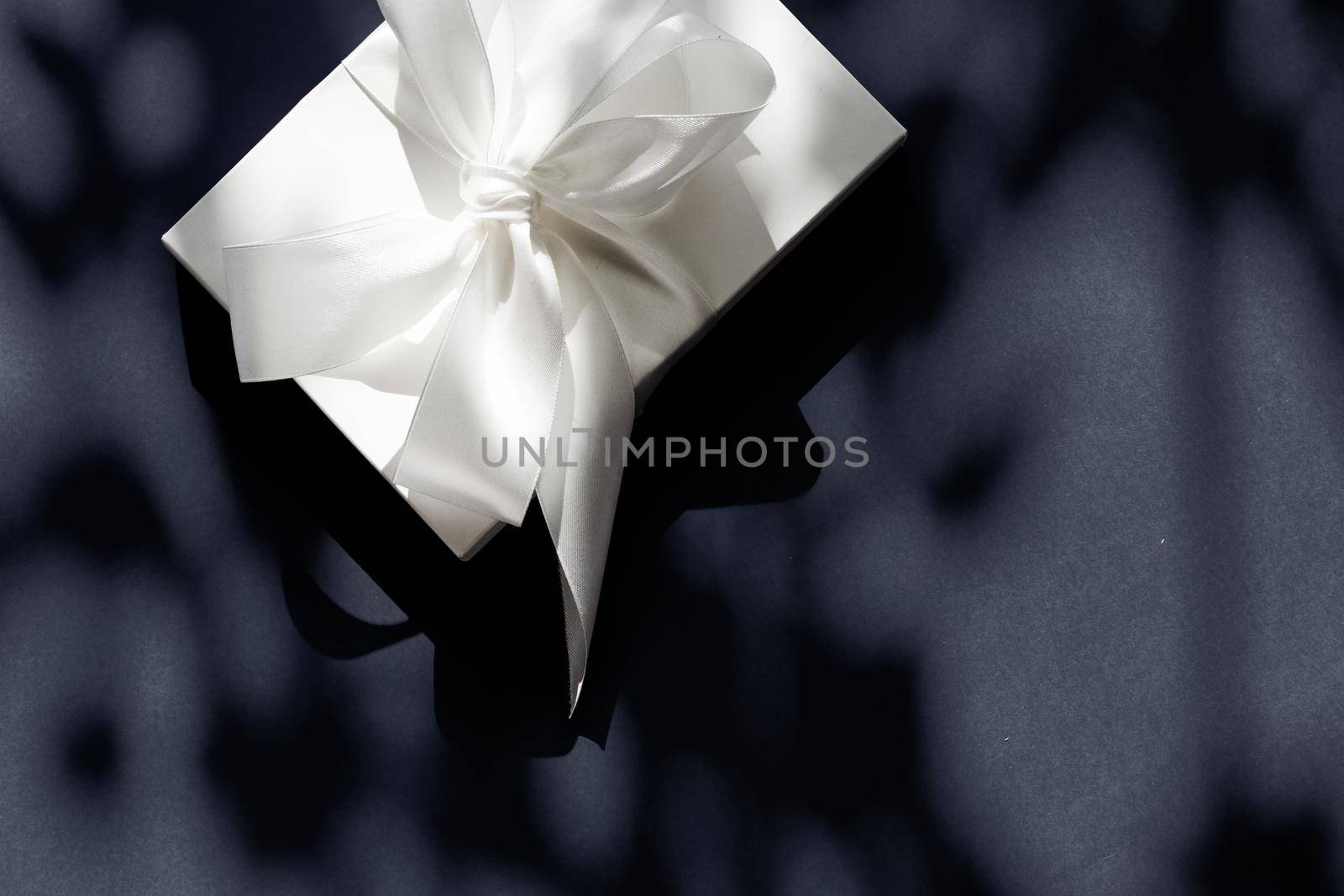 Luxury holiday white gift box with silk ribbon and bow on black background, luxe wedding or birthday present by Anneleven