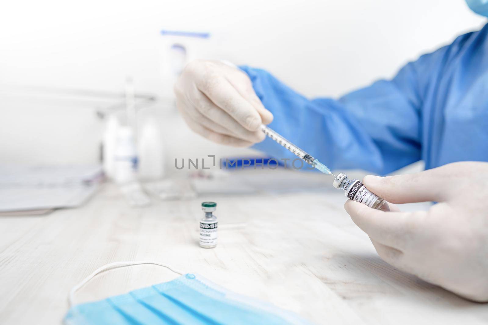 Hands close-up shot of senior doctor, nurse or healthcare worker in personal protective kit sitting at hospital or health clinic desk preparing syringe for vaccination amid Coronavirus or Covid-19