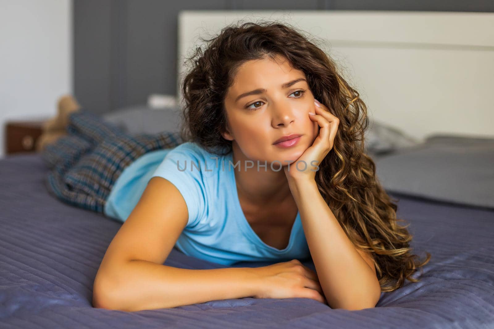 Beautiful sad woman lying on her bed and thinking about something.