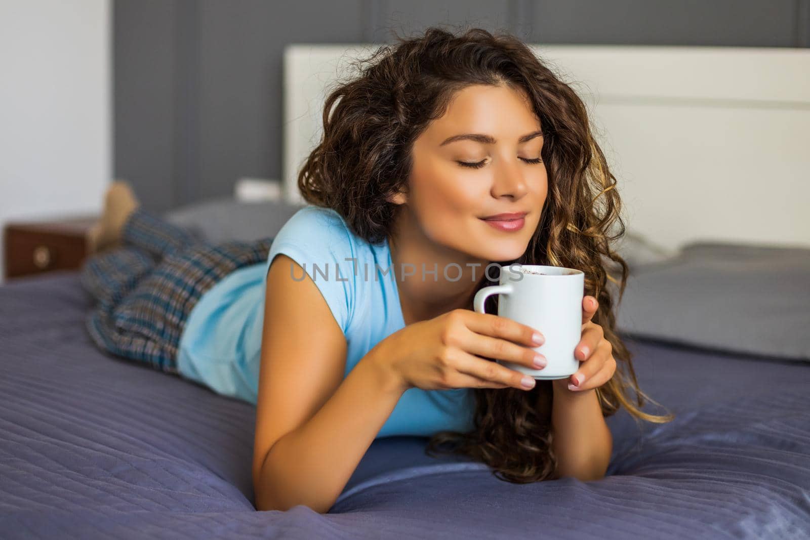 Beautiful woman enjoys drinking coffee in her bed.