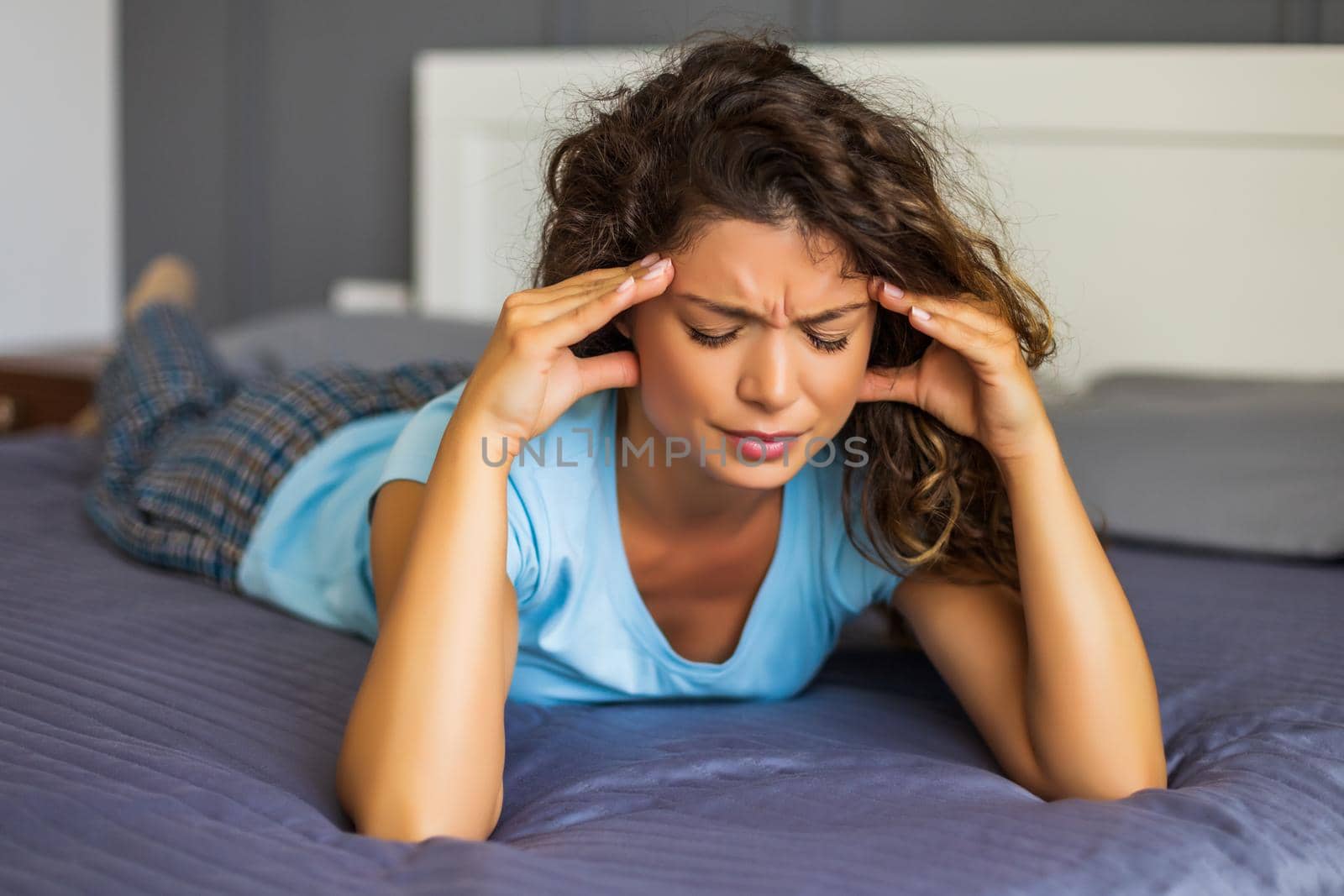 Worried woman having strong headache while lying on her bed in bedroom.
