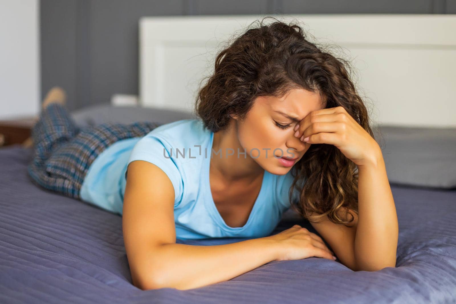 Worried woman having strong headache while lying on her bed in bedroom.