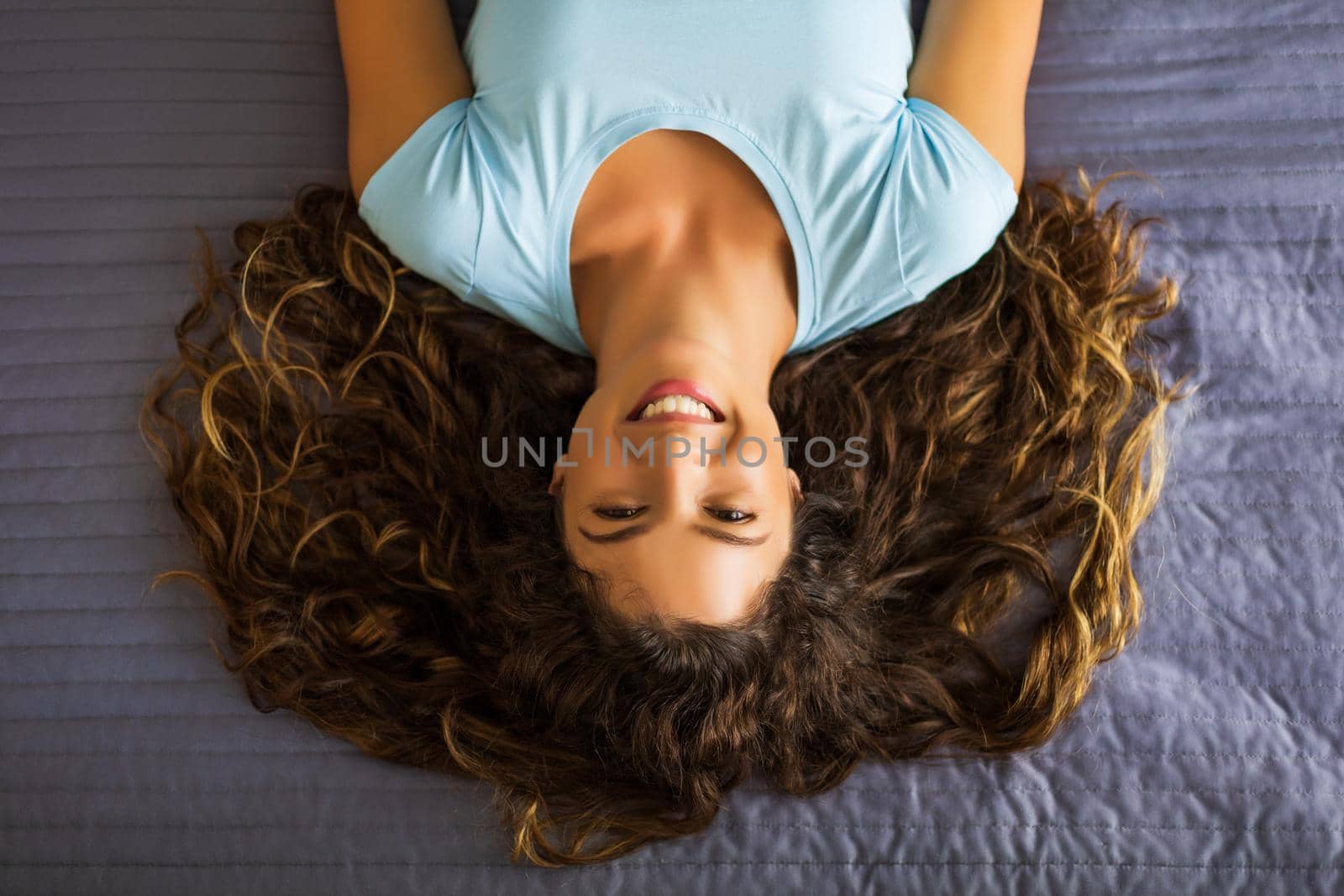 Portrait of beautiful woman with long curly hair resting  on bed.