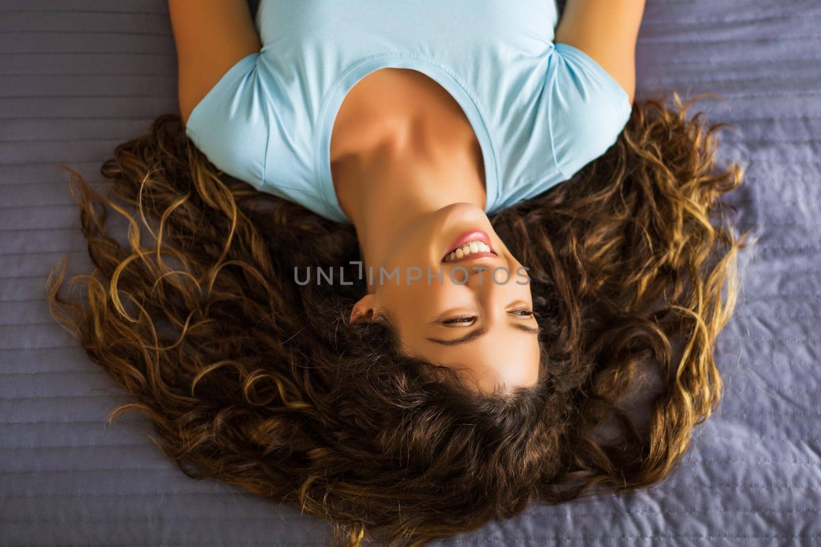 Portrait of beautiful woman with long curly hair resting  on bed.