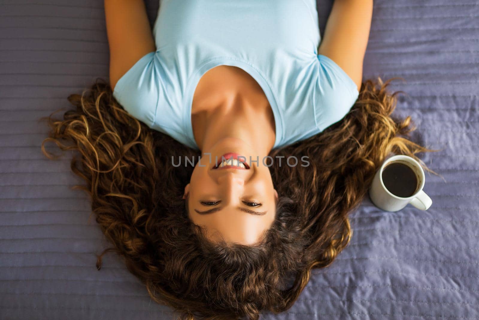 Woman lying down on her bed with cup of coffee by Bazdar