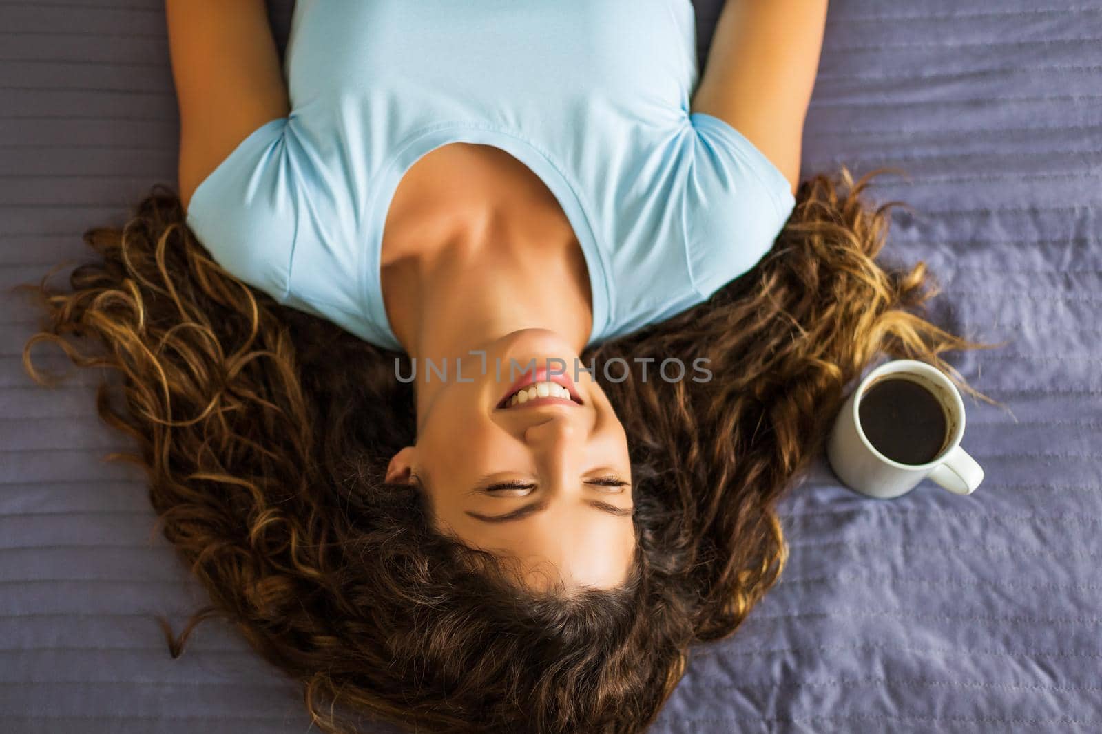 Beautiful woman lying down on her bed with cup of coffee.