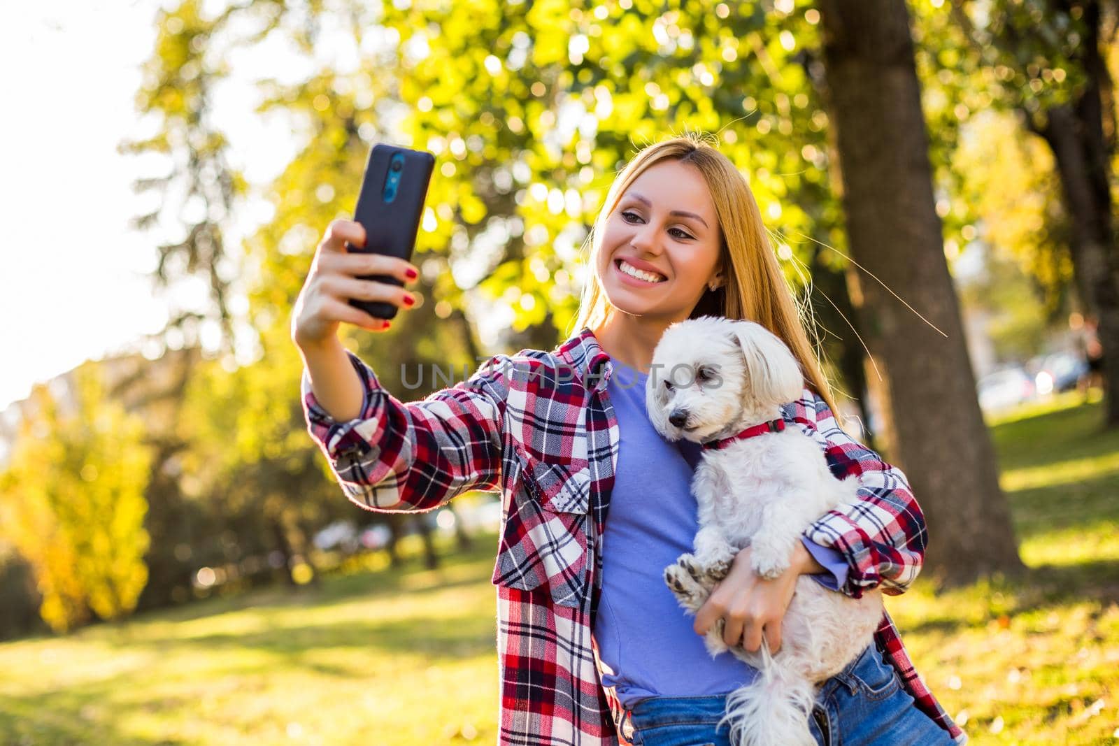Beautiful woman taking selfie with her Maltese dog in the park.