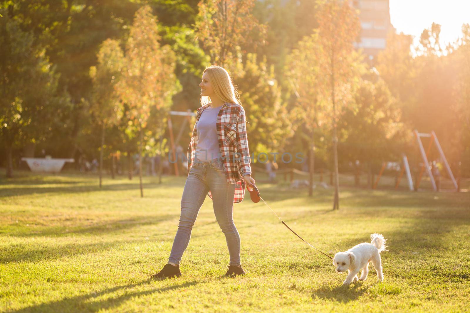 Beautiful woman walking with her Maltese dog in the park.