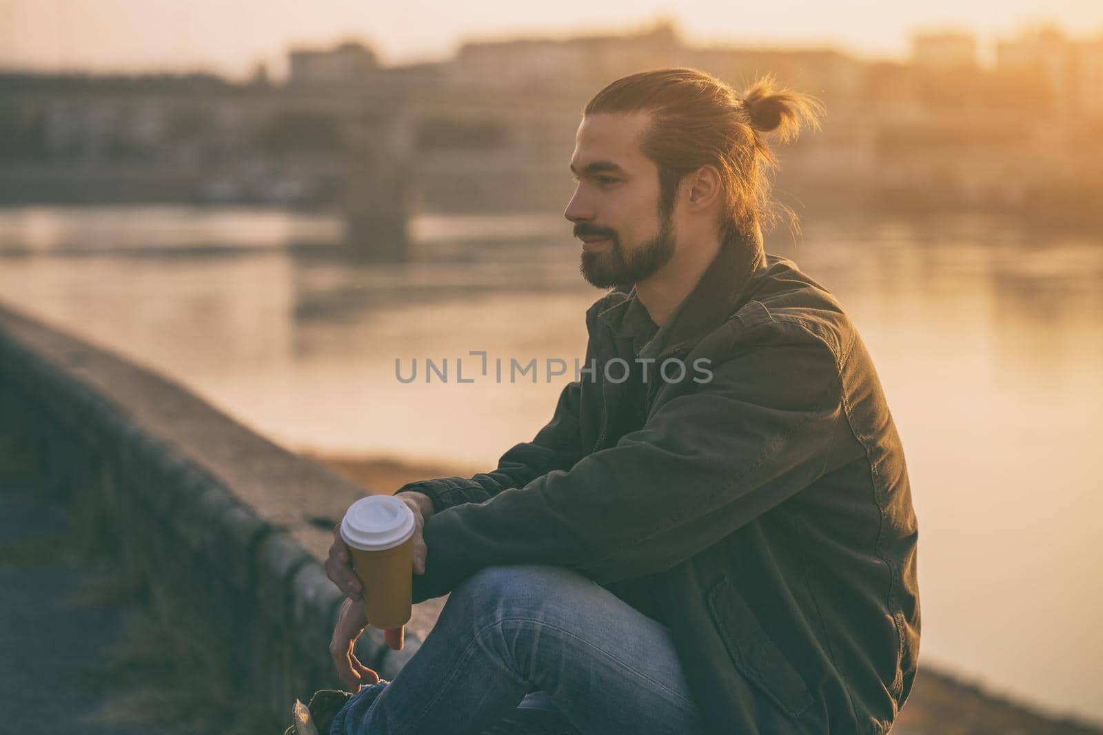 Handsome modern businessman enjoys drinking coffee and resting by the river.