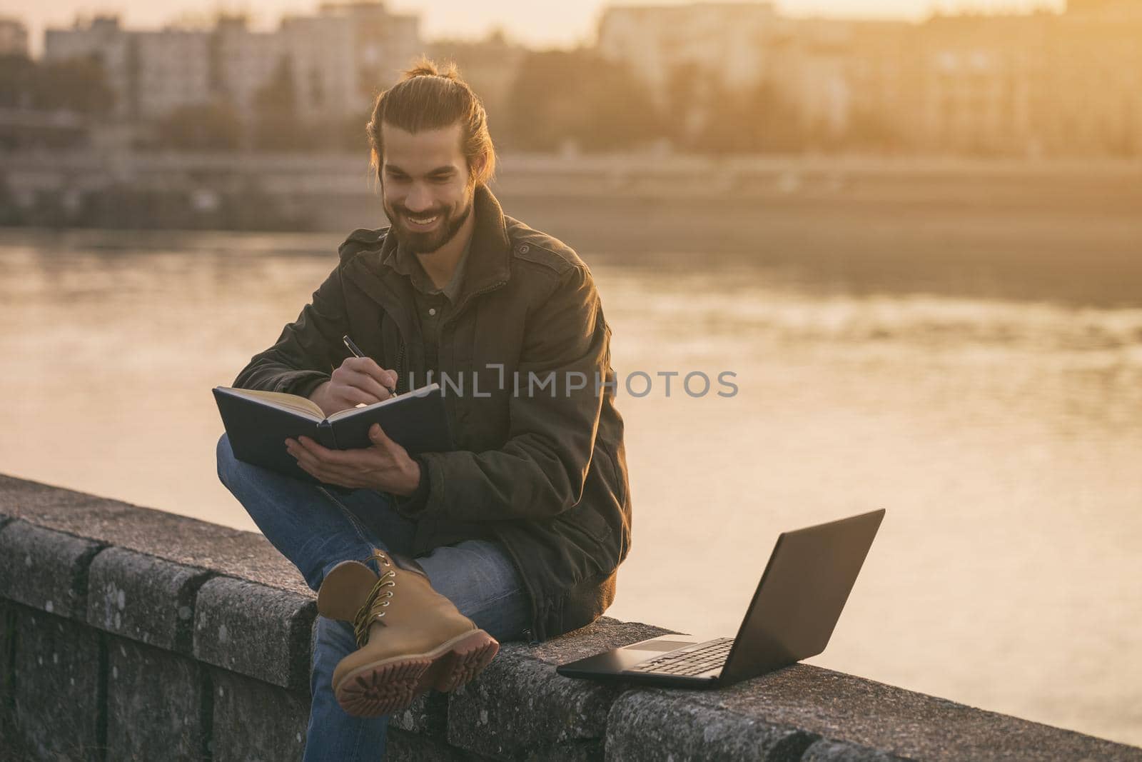 Handsome businessman using personal organizer and laptop while sitting by the river.