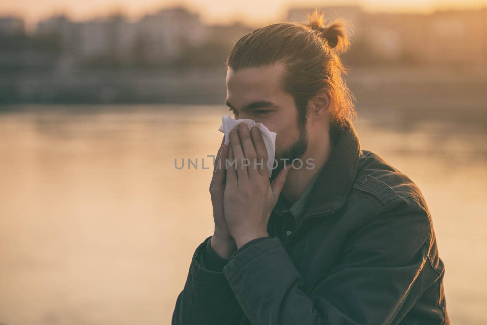 Modern businessman is blowing nose while sitting by the river.