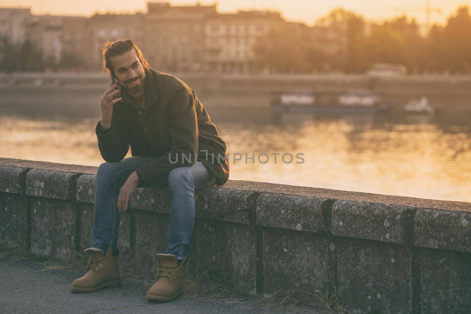 Handsome modern businessman using phone while sitting by the river.