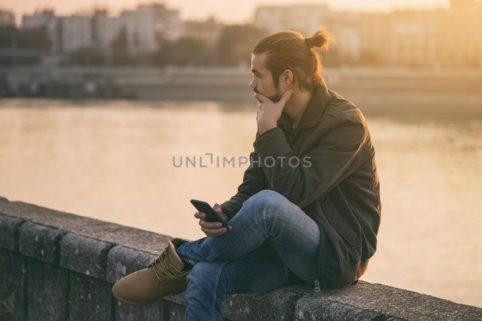 Sad businessman holding phone while sitting by the river.