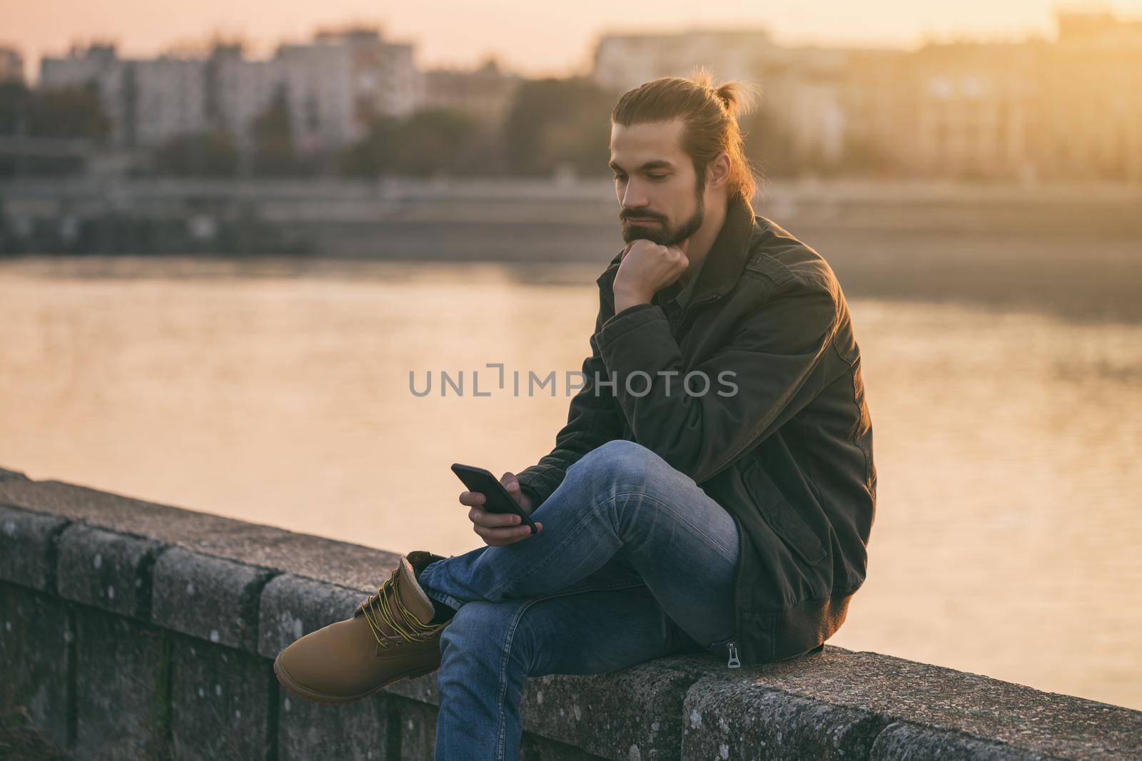 Sad businessman holding phone while sitting by the river.