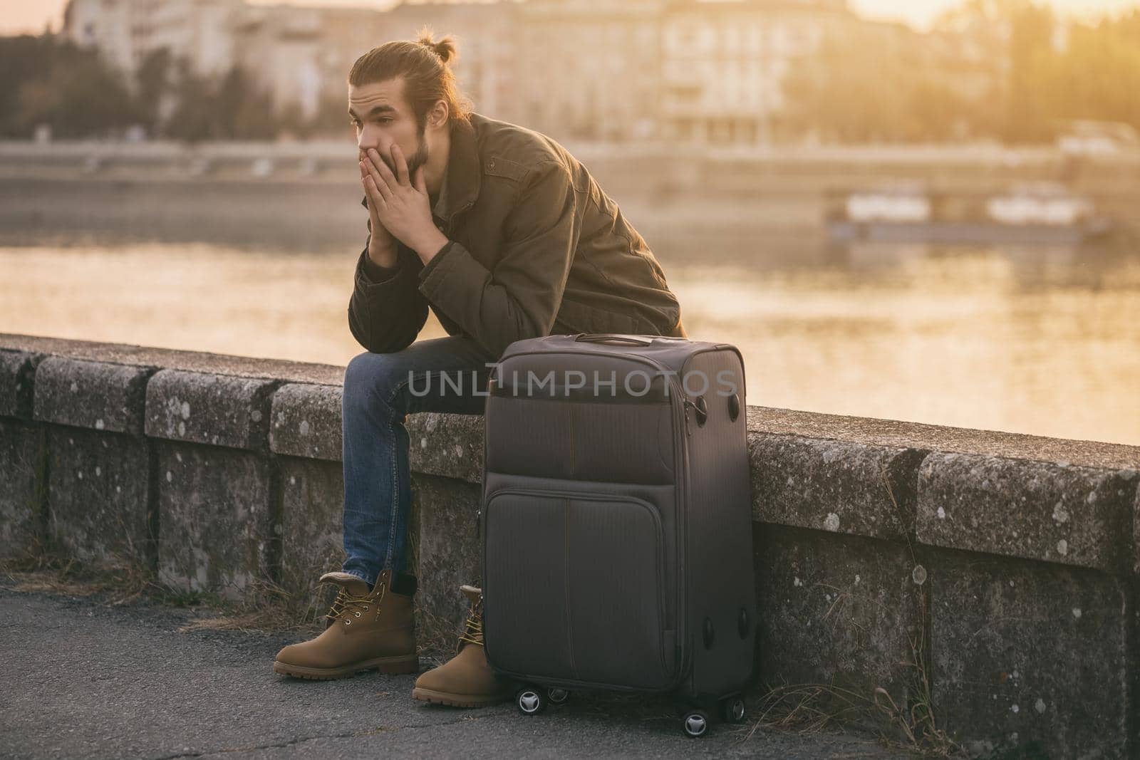 Desperate businessman with suitcase sitting lost by the river.