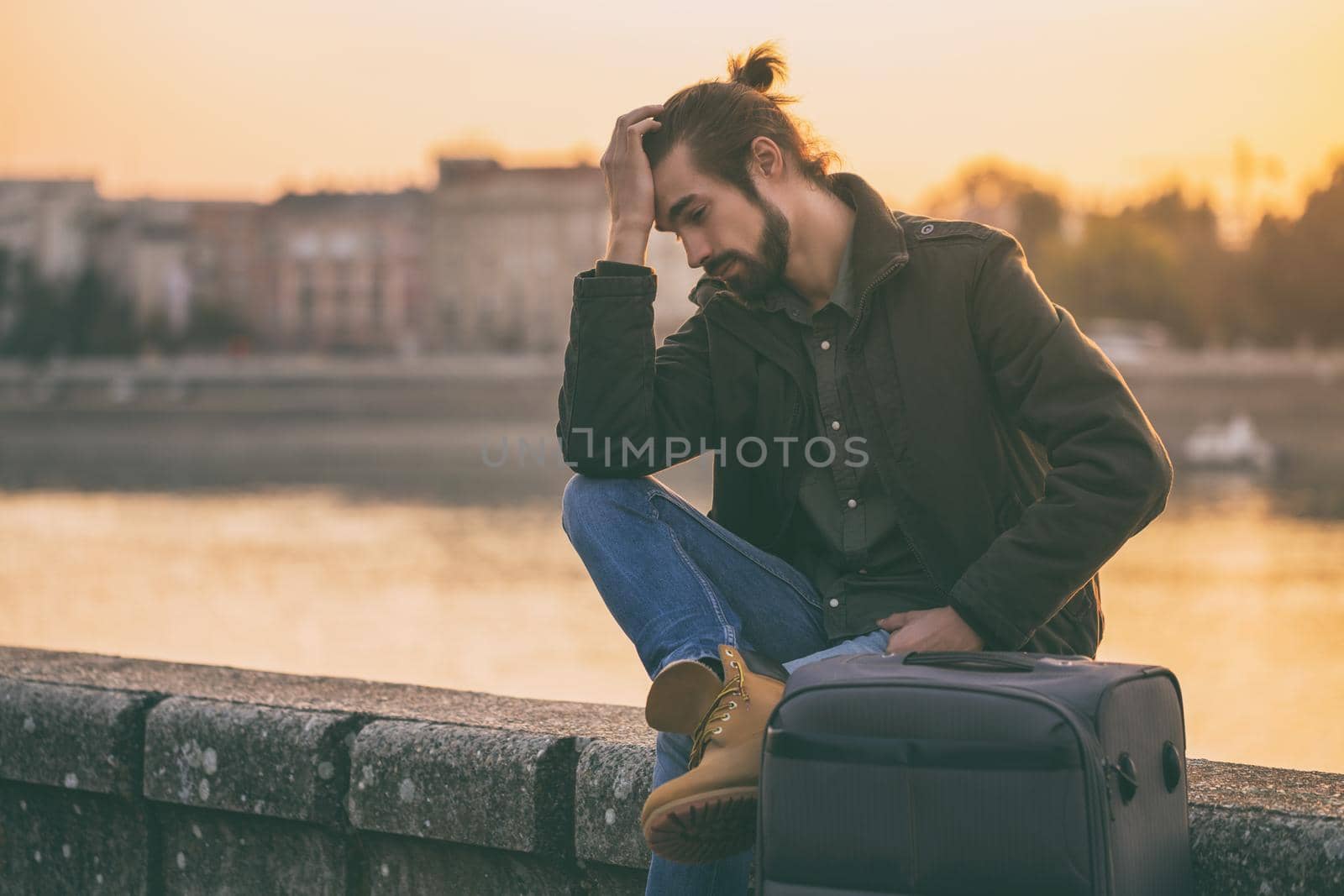 Desperate businessman with suitcase sitting lost by the river.