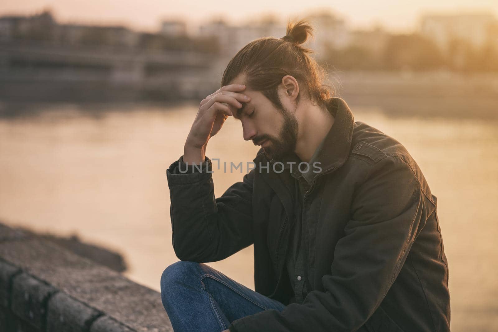 Young modern businessman is having a headache while sitting by the river.