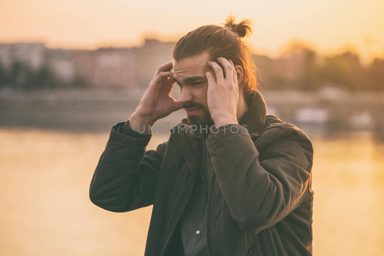 Young modern businessman is having a headache while sitting by the river.