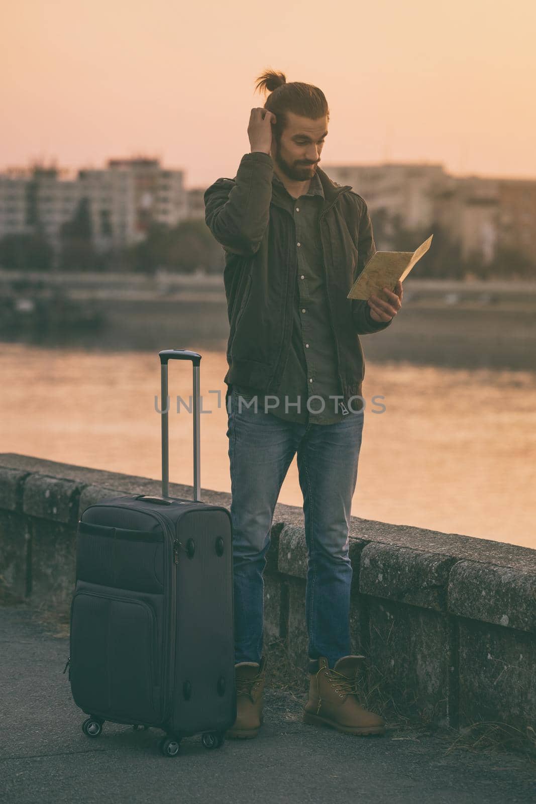 Confused businessman with suitcase and city map standing lost by the river.