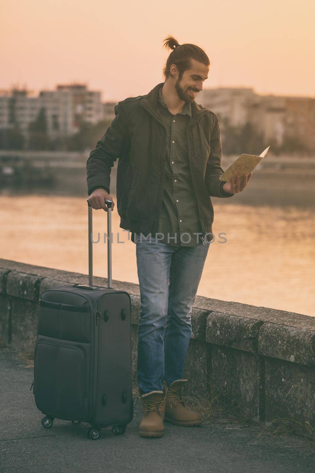 Handsome businessman with suitcase holding map of the city and standing by the river.