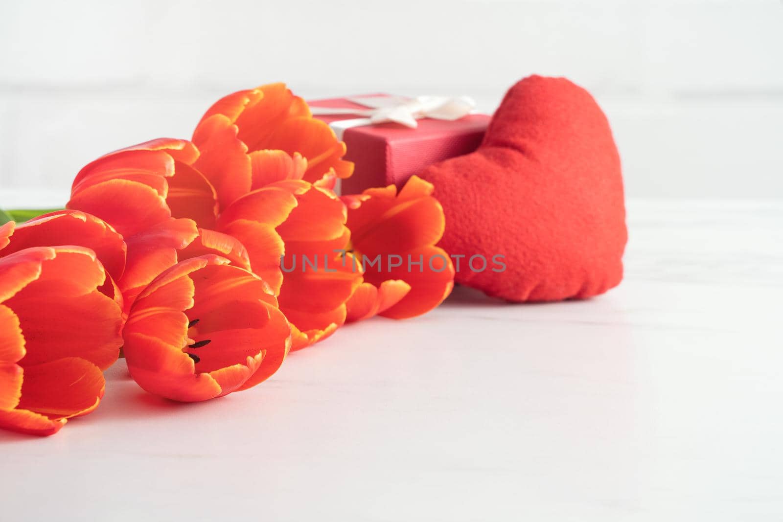 Mother's Day gift. Close up design concept of red tulip bouquet with gift and heart shape on white table background and brick wall decoration.
