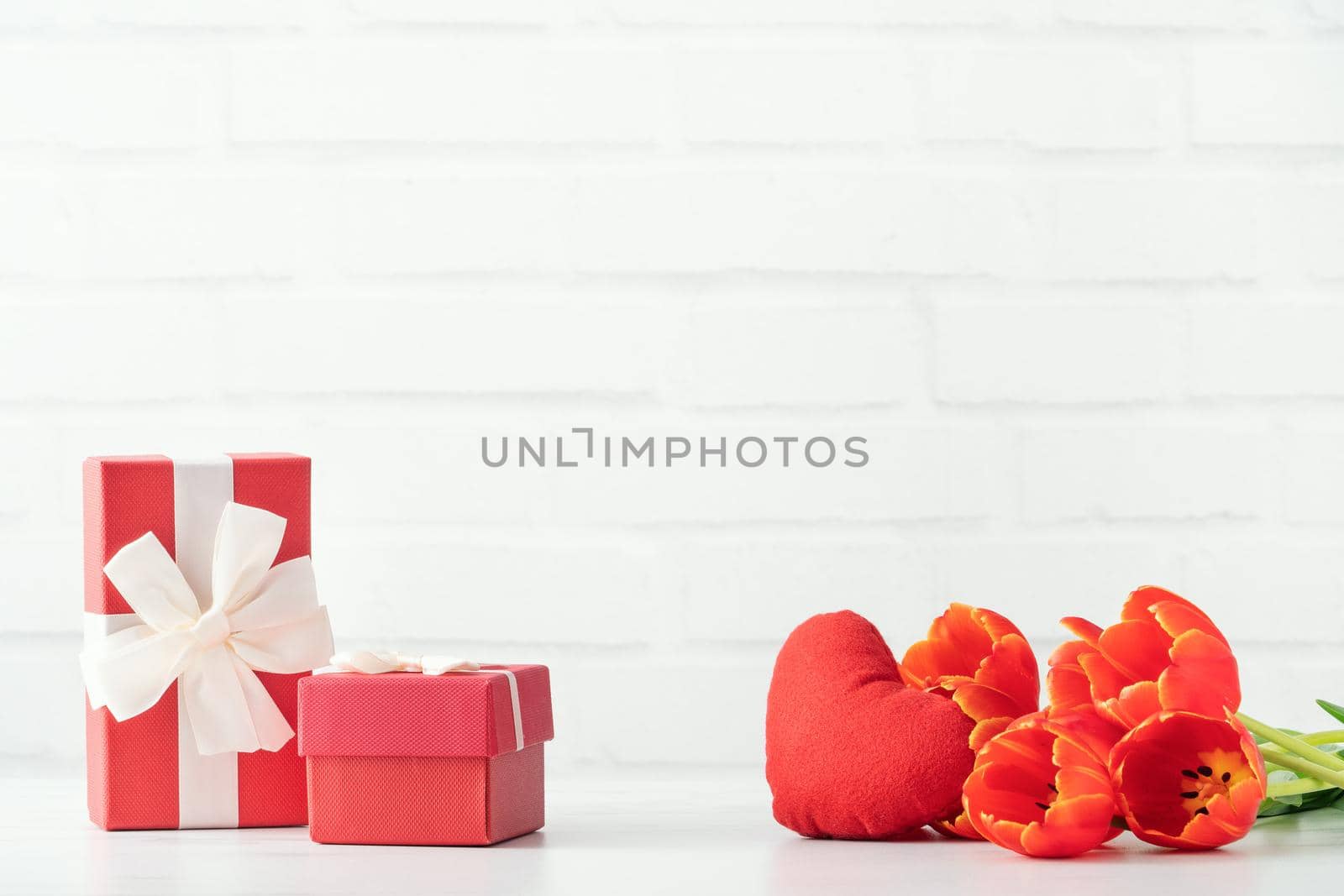 Mother's Day gift. Close up design concept of red tulip bouquet with gift and heart shape on white table background and brick wall decoration.