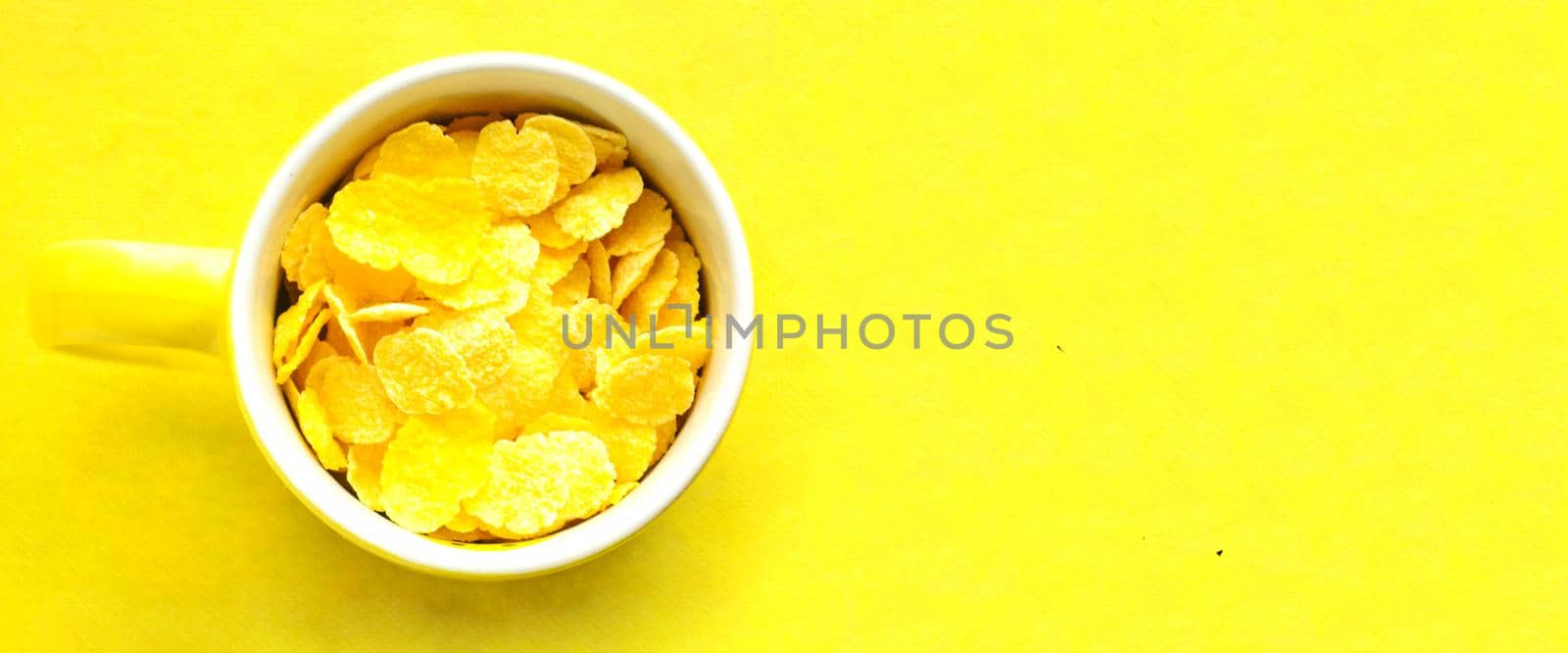 Top view, yellow cup with cornflakes on bright yellow background.