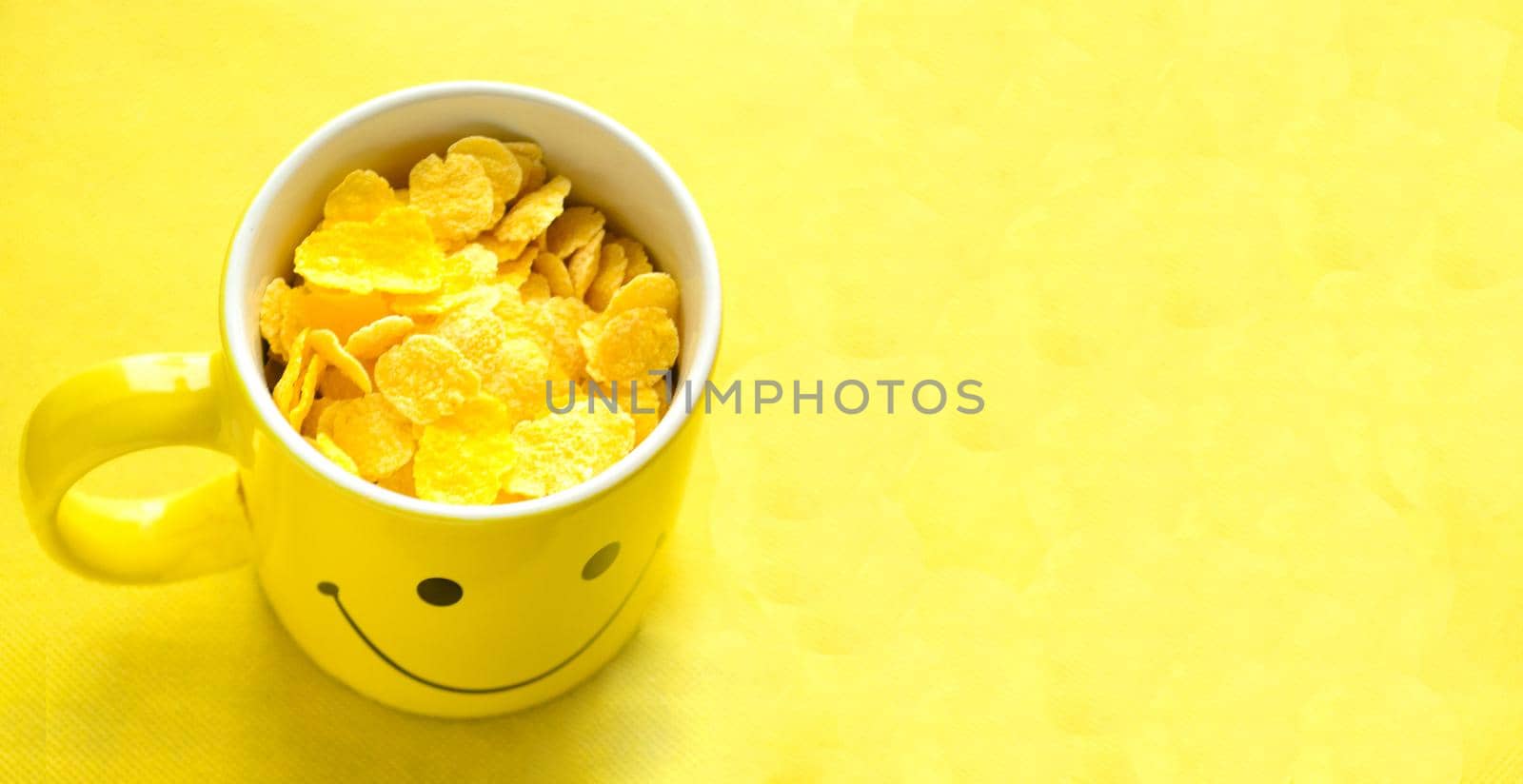 Top view,Happy yellow cup with cornflakes on bright yellow background.A cup with happy emoticon for sunny summer.