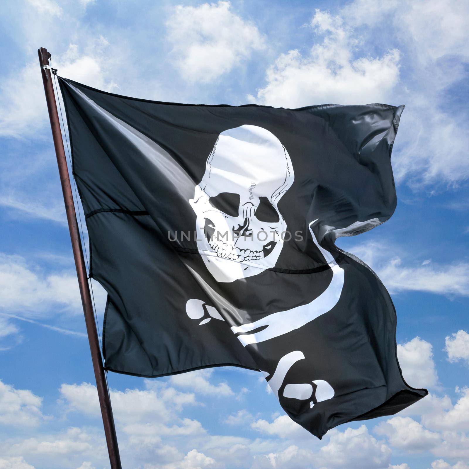 Pirate flag against blue sky. Pirates flag in the wind, depicting the skull and crossbones as a symbol of pirates. Space for text.