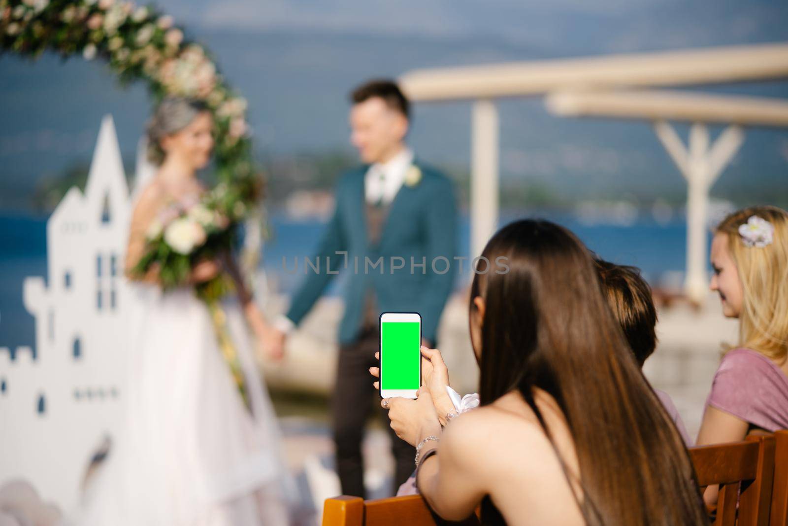 Young girl photographs the bride and groom on a smartphone. Blank screen. High quality photo