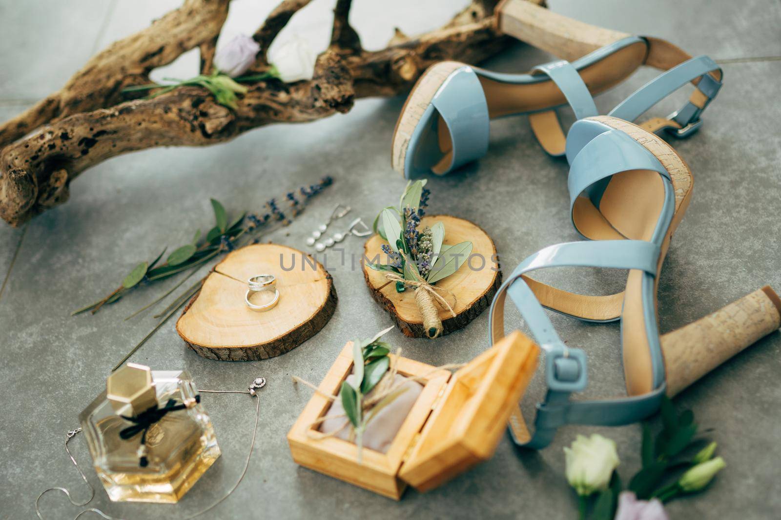 Wedding rings lie in a wooden box surrounded by sandals with heels, perfume, flowers and twigs on the floor. High quality photo