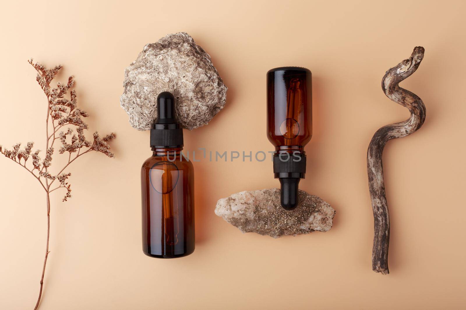 Top view of skin serums in dark bottles against beige background with stones and dry flowers by Senorina_Irina
