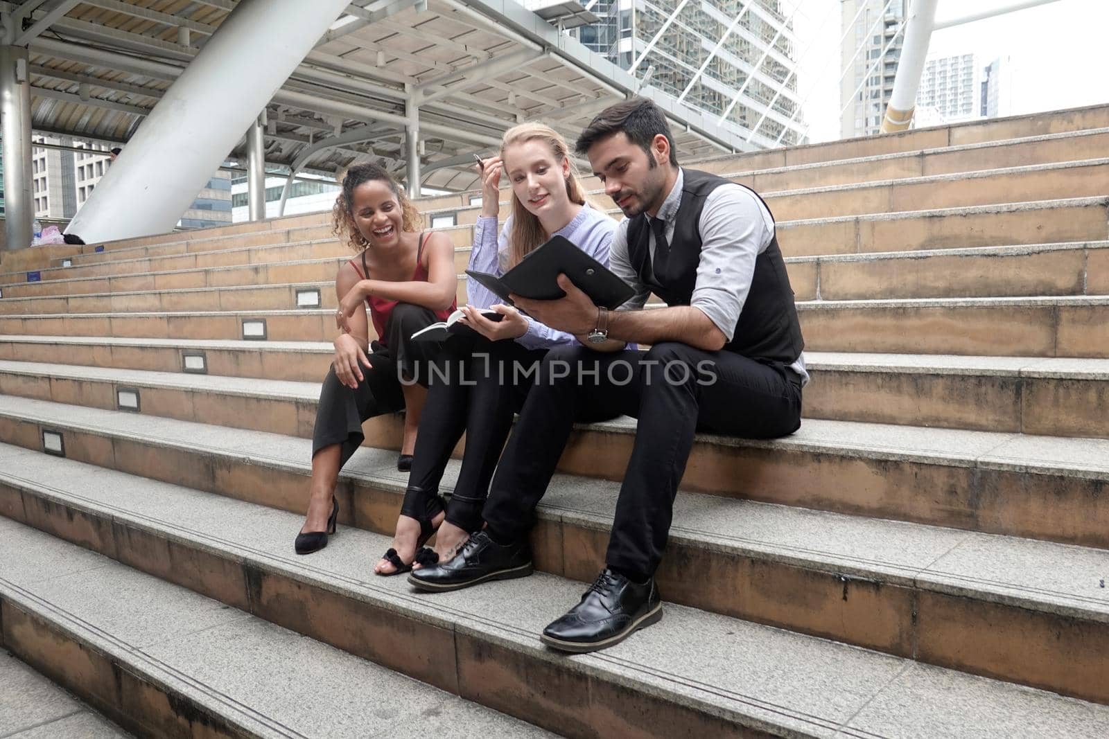 Group of businesspeople using a digital tablet together in front of office building windows overlooking the city