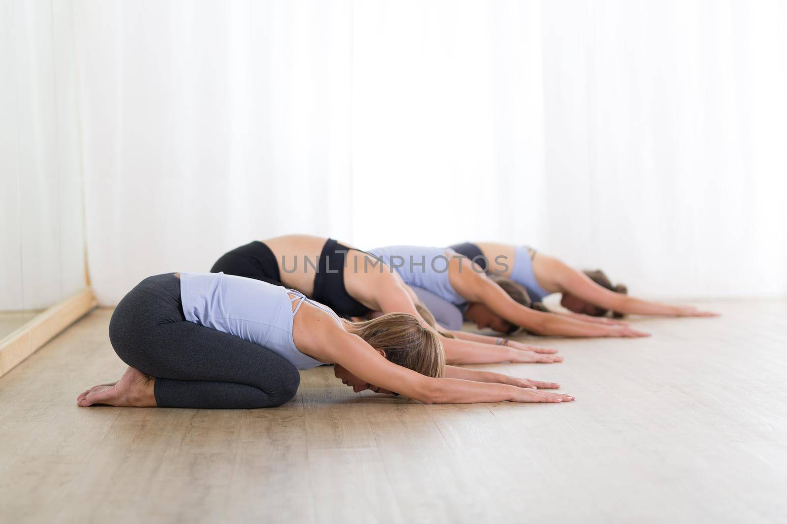 Group of young sporty women in yoga studio, practicing yoga. Healthy active lifestyle, working out indoors in gym.