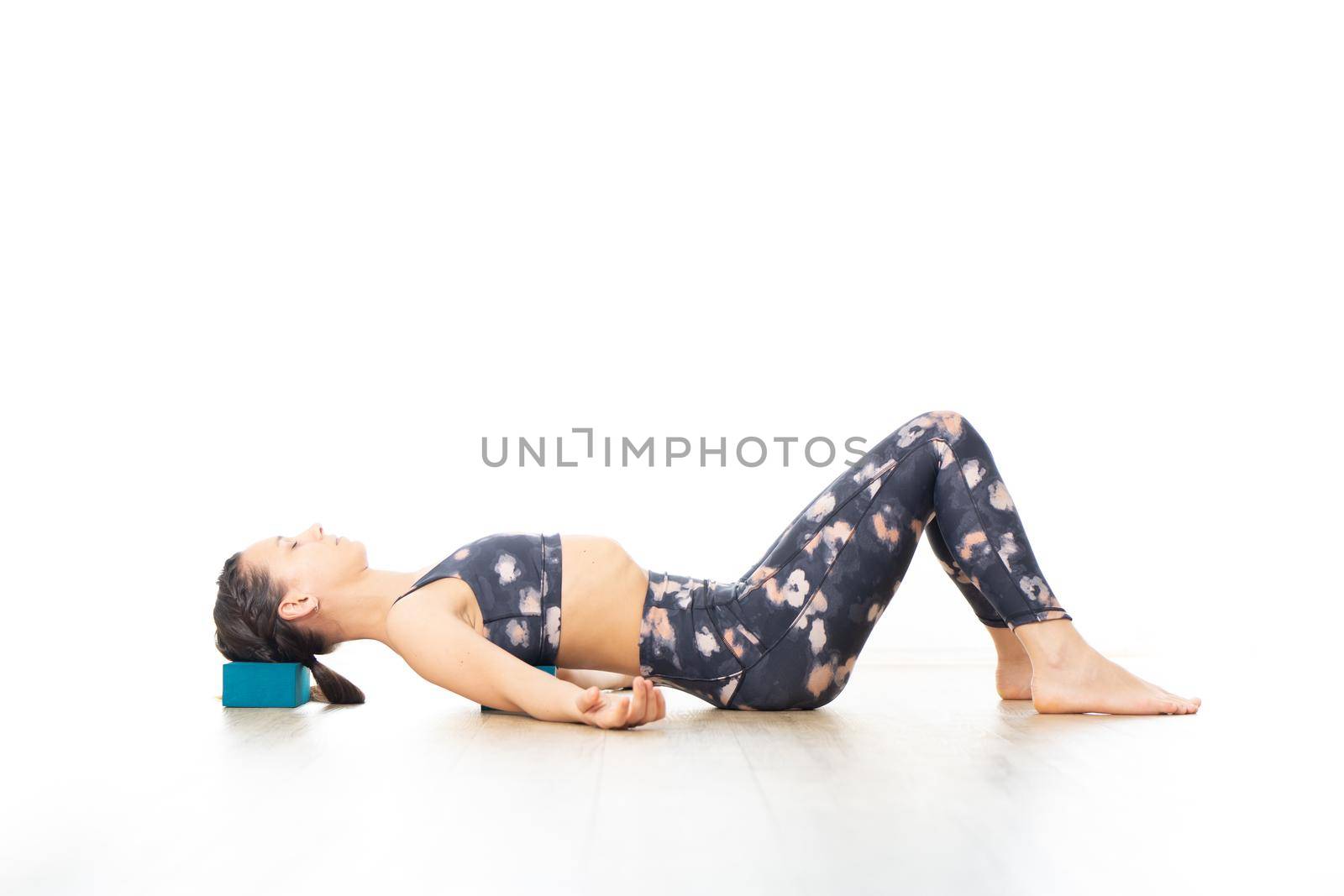 Young sporty attractive woman in bright white yoga studio, stretching and relaxing during restorative yoga using gadget. Healthy active lifestyle.