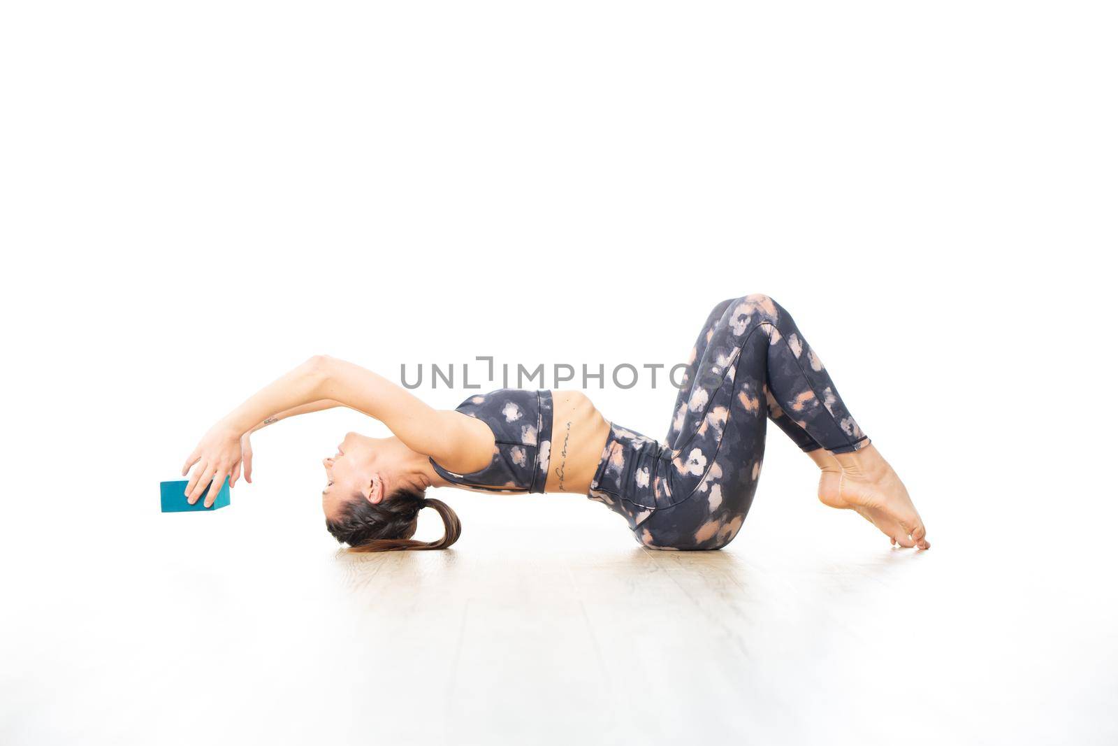 Young sporty attractive woman in bright white yoga studio, stretching and relaxing during restorative yoga using gadget. Healthy active lifestyle.