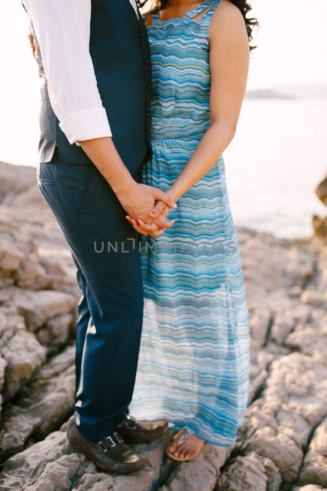Man in a suit and woman in a long dress with an ornament stand on a stone shore holding hands. High quality photo