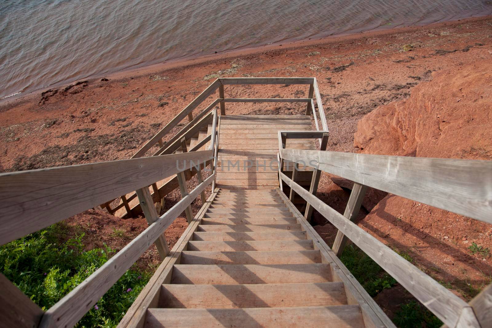 A staircase flight made of wood leading down to red clay beach below 