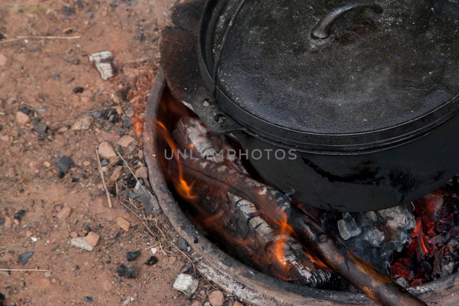 Coals and flames on a fire pit with a black cauldron oven 