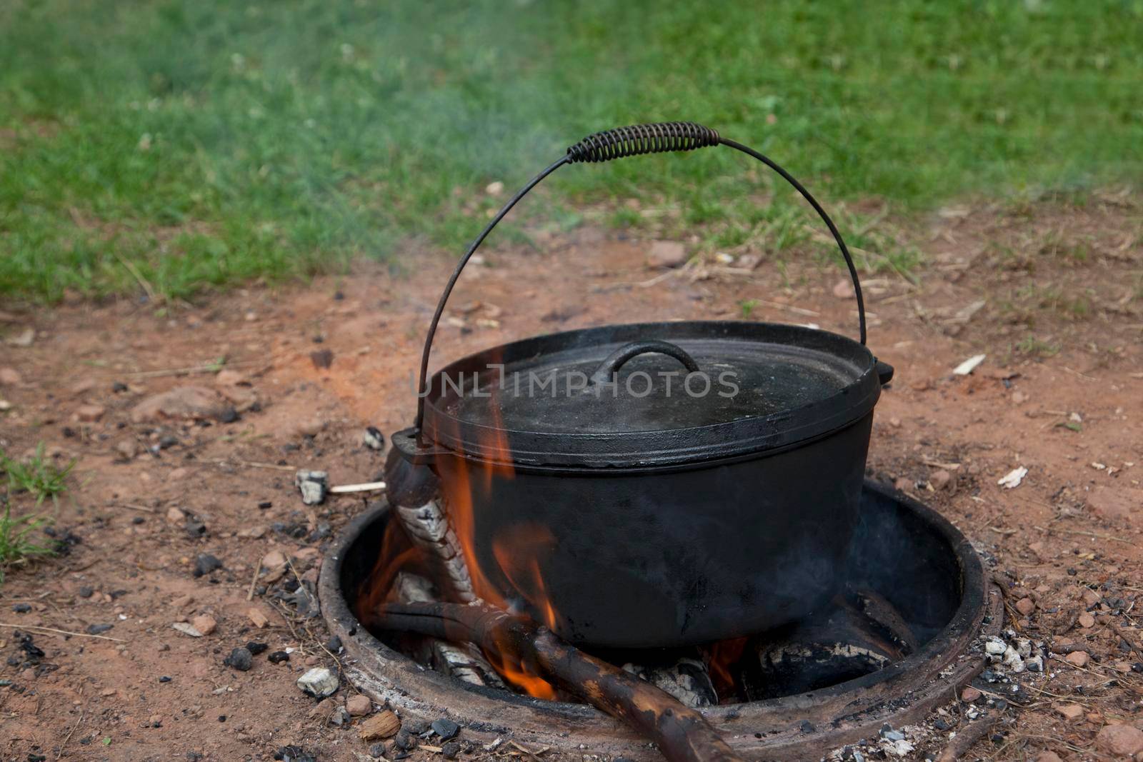 Over a pit, a black cauldron with flames cooks a campfire meal