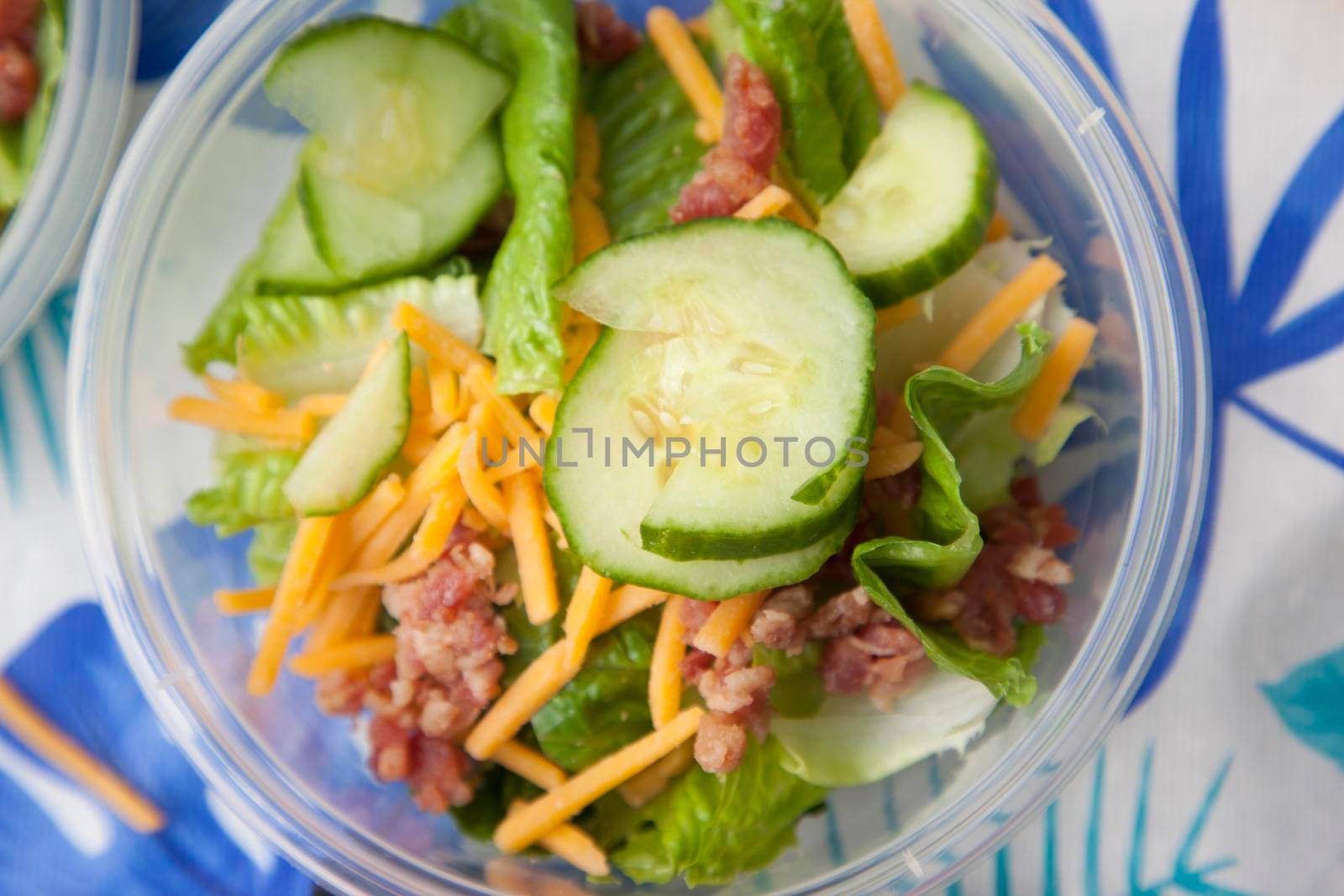 Plastic dish with salad, bacon, cheese and cucumbers 
