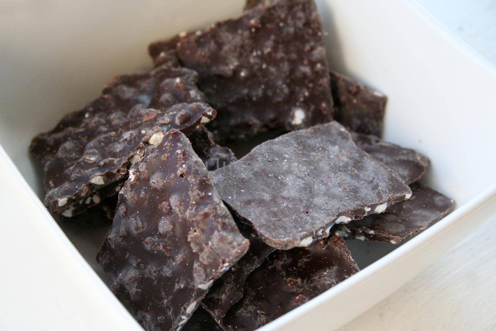 Tasty looking thin slivers of chocolate bark with nuts inside a white bowl 
