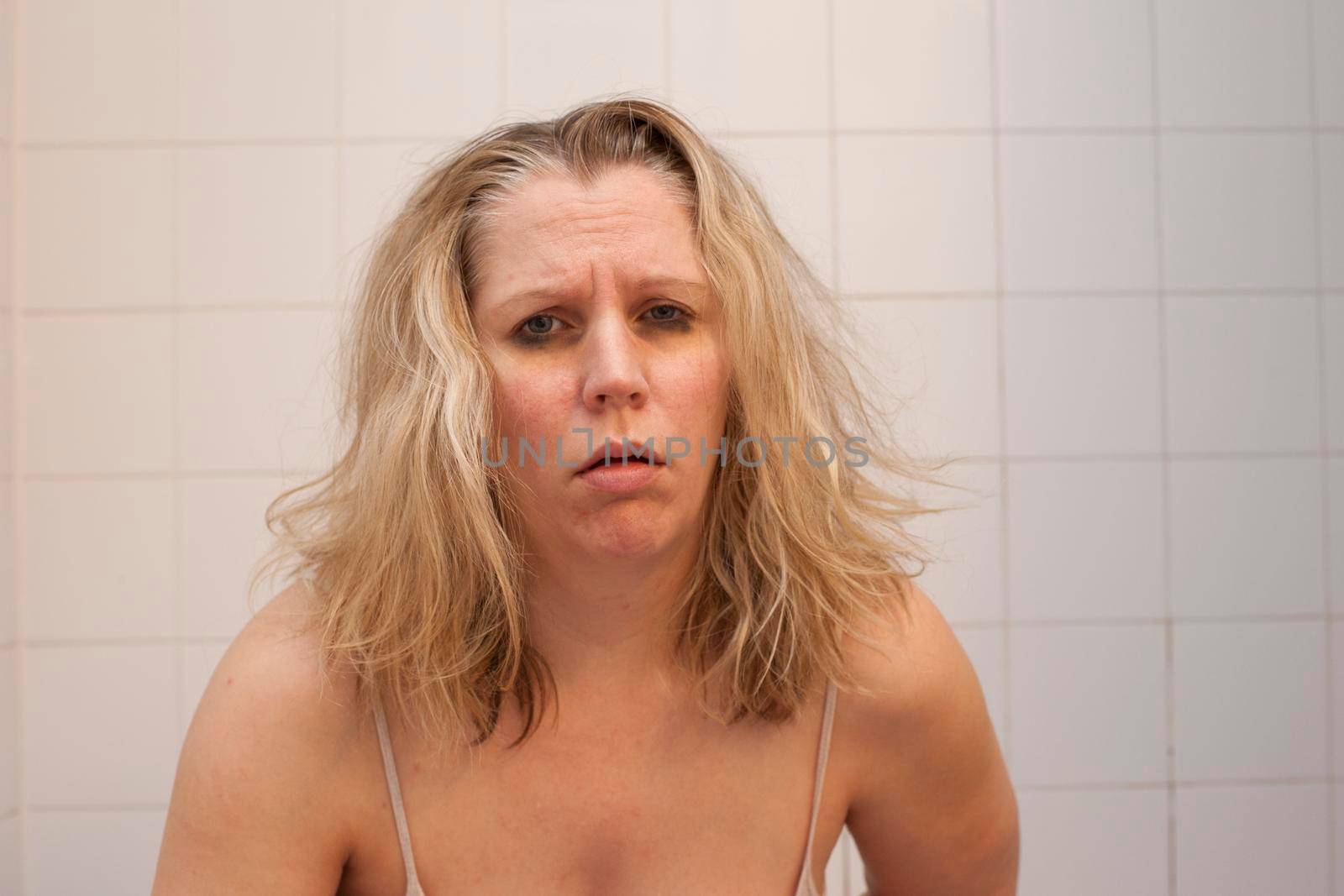 Woman with black bruised eyes and messy hair looks like she is ready to be sick or throw up 