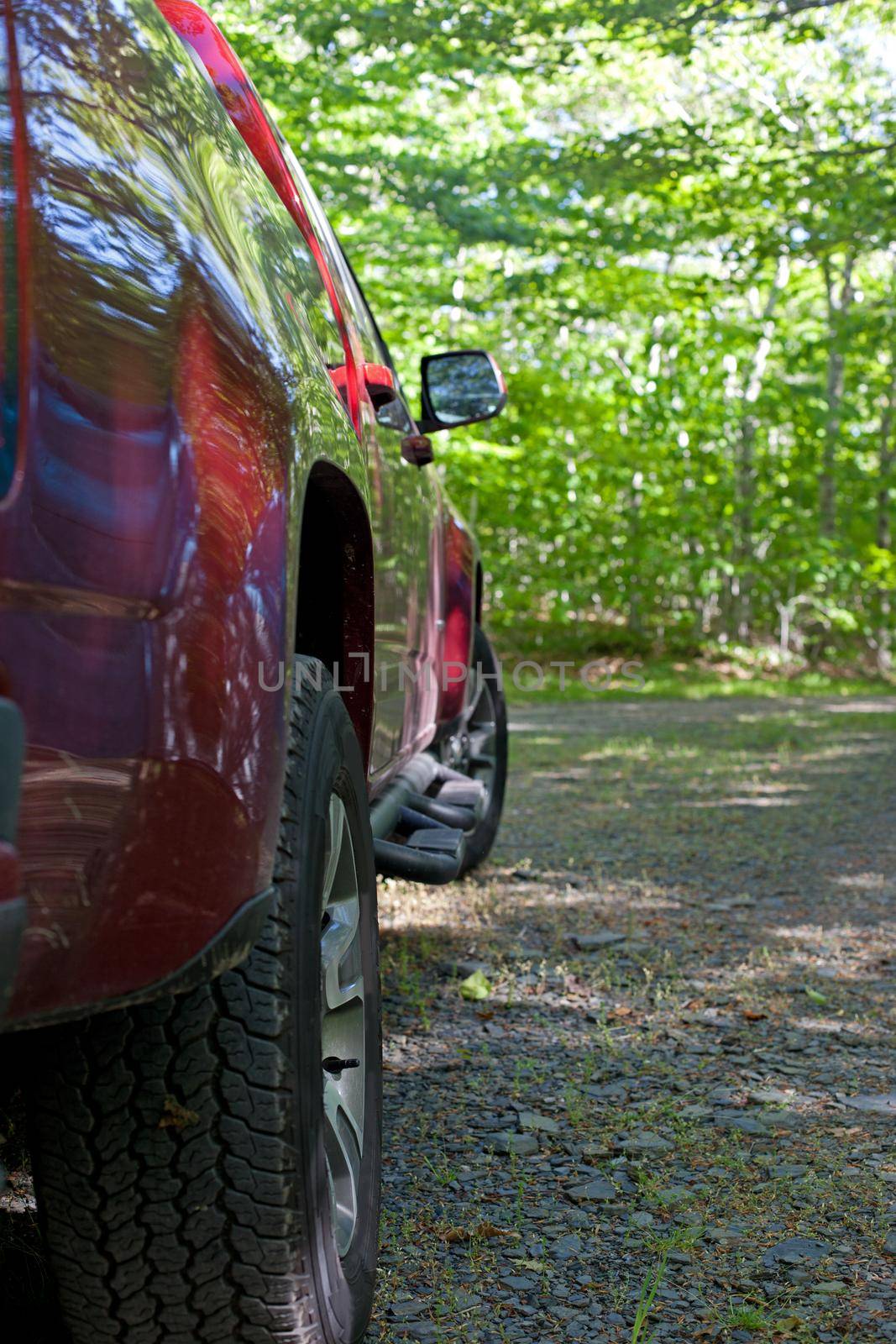 A red truck parked at a wooded lot, extreme focus on the back tire and back end of vehicle 