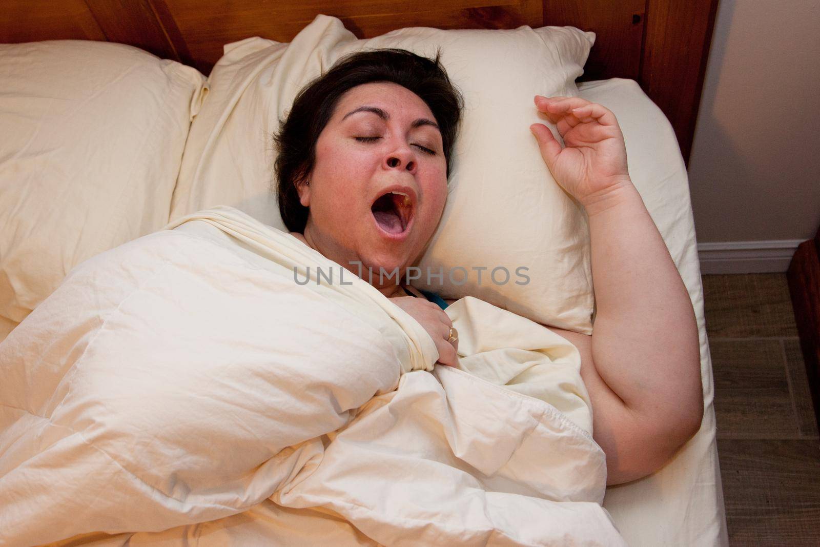 A woman is tucked under covers with a big yawn 