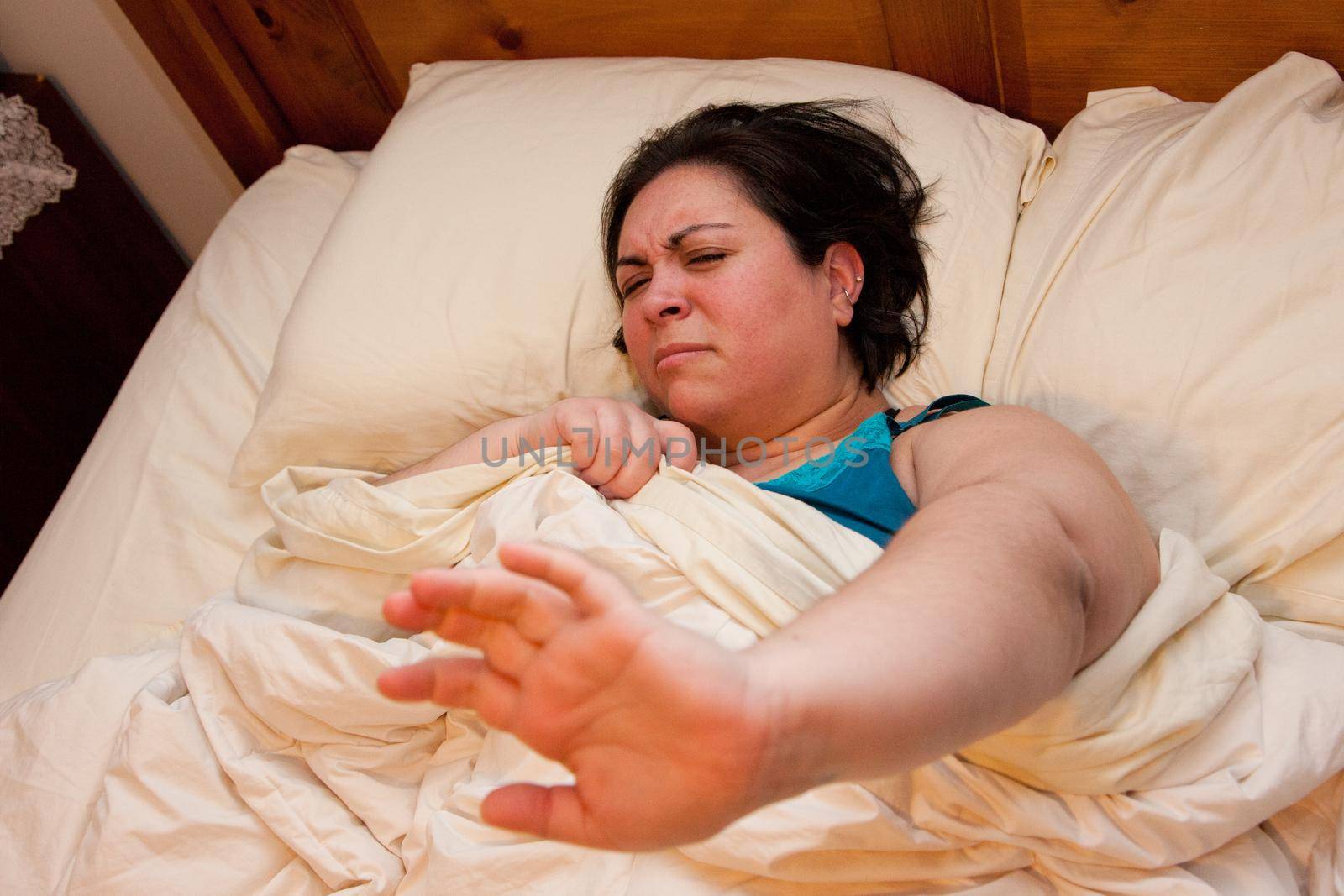 Cranky woman in bed holds out her hand to be left alone to sleep 